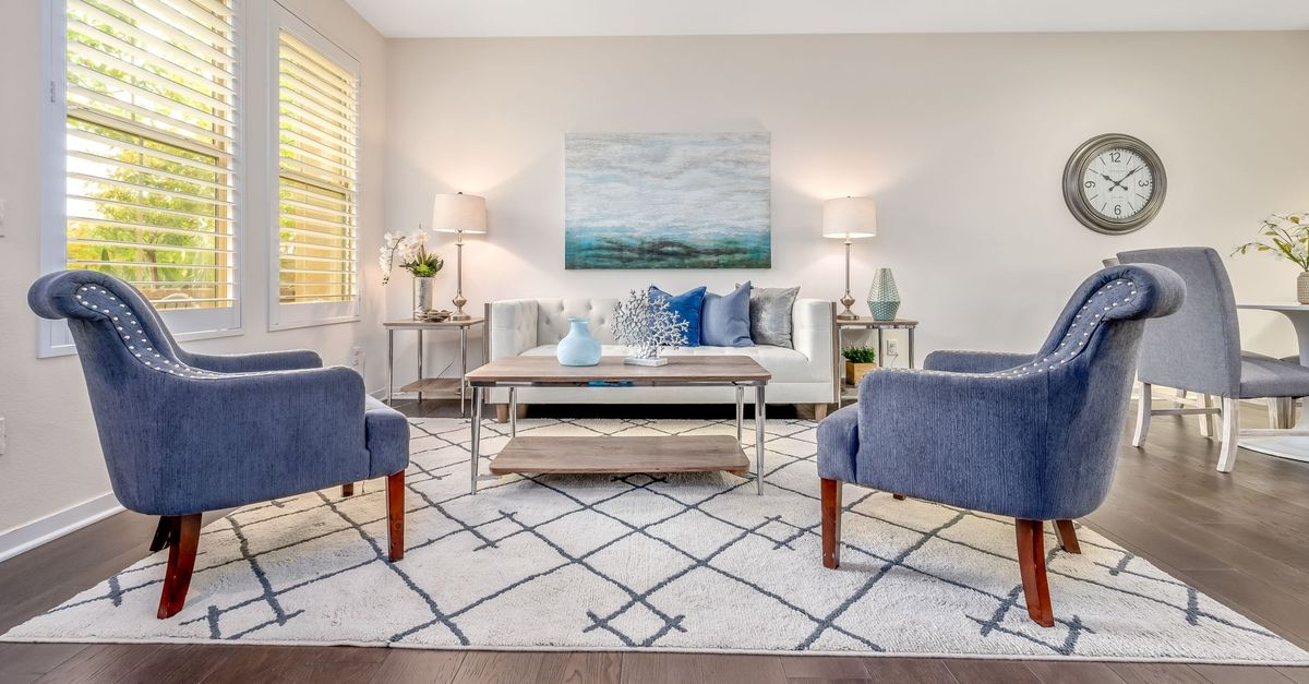 Un salon lumineux aménagé avec deux fauteuils bleus, un canapé clair et un tapis à motifs